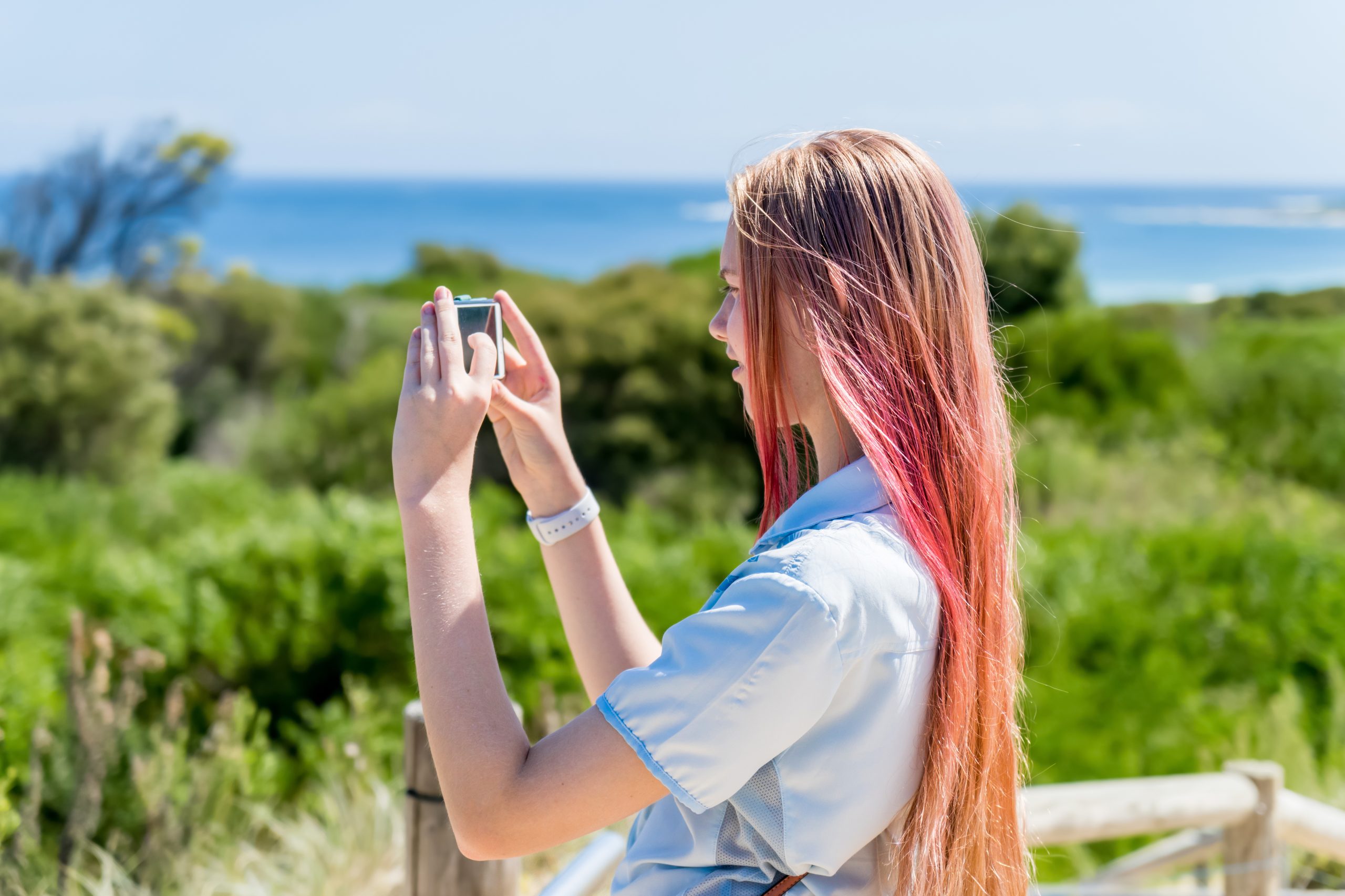 Generation Z teenage girl with pink ombre colored hair making photo and video of beautiful landscape on a phone