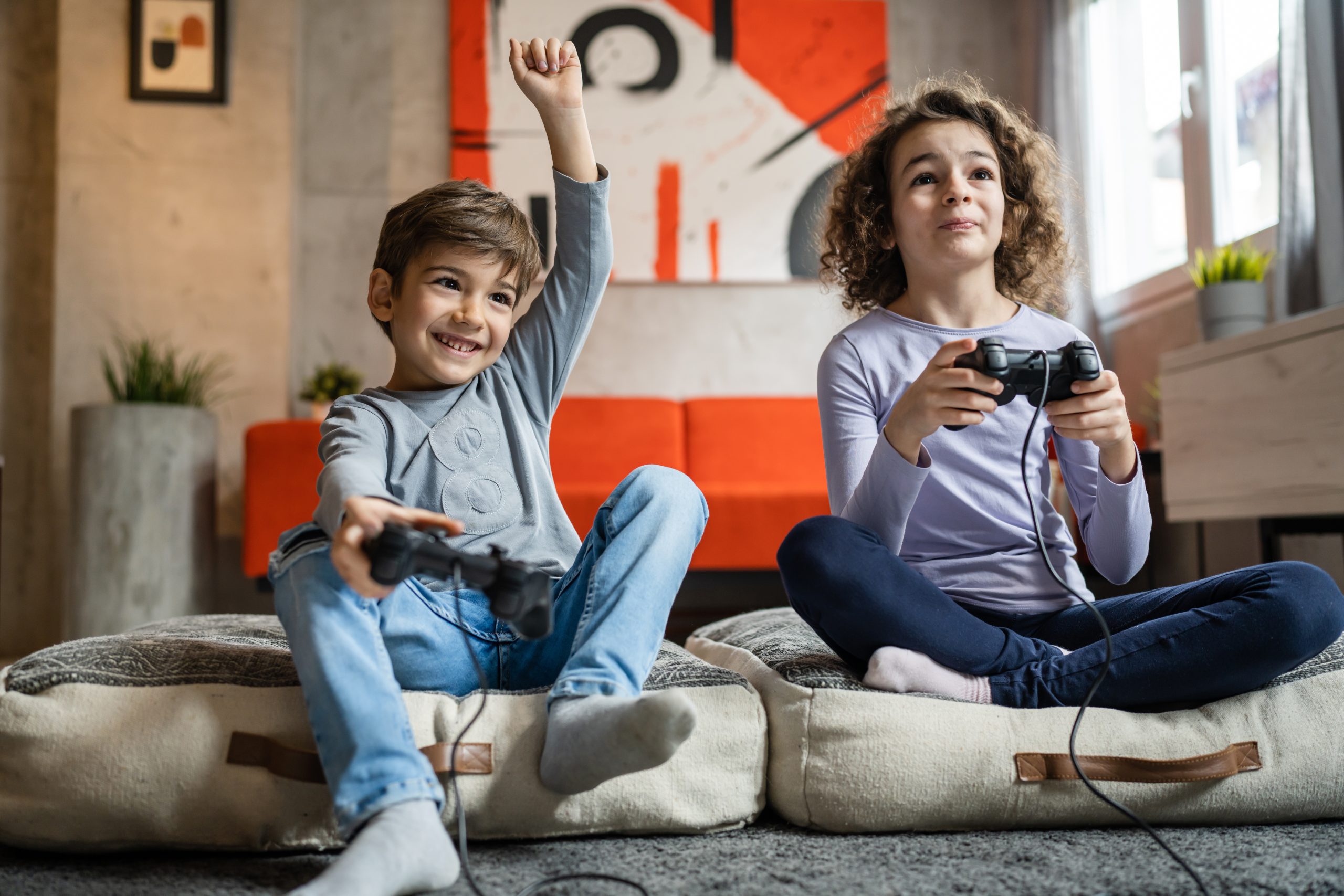 Two children small caucasian brother and sister happy children siblings boy and girl playing video game console using joystick or controller while sitting at home boy is winning