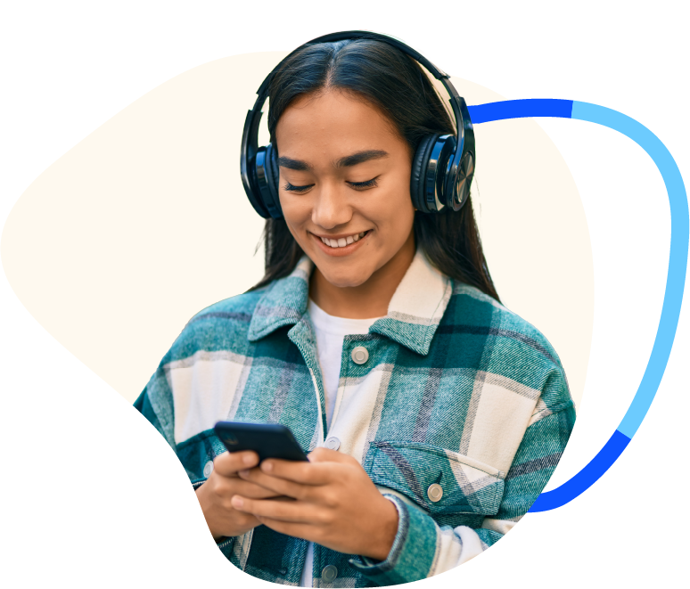 Teenage girl in chequered shirt with black hair looking at smartphone and smiling with over the ear headphones on