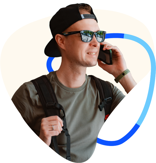 Teenage boy with backwards cap, sunglasses and backpack on talking on the phone and smiling