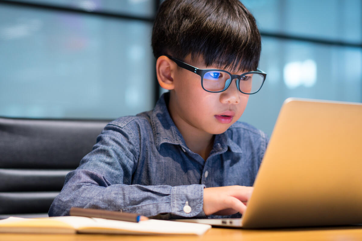 Young boy with glasses doing homework on a laptop at home