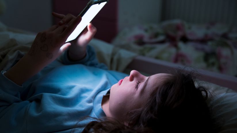 Photo of teenager looking at smartphone in the dark